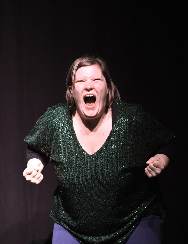 Eine Frau ballt die Fäuste zusammen und schreit laut. Sie trägt ein grünes T-Shirt mit Glitzer.